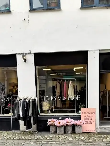 Butikken sett fra brosteinsgaten, med klesstativ og blomsterbøtter utenfor.
